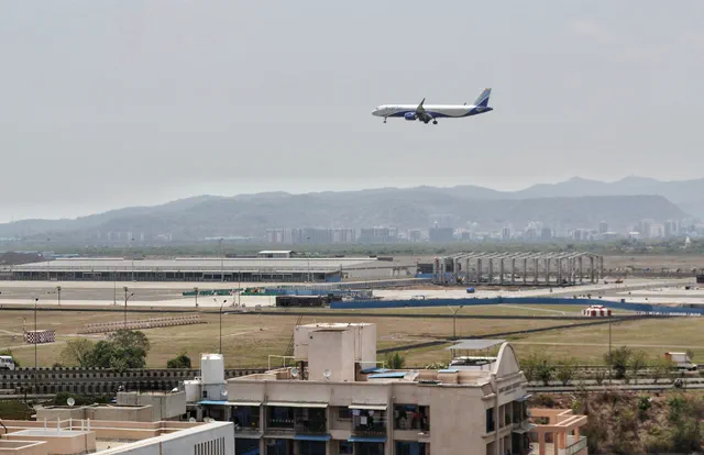 An airliner on final approach over the Navi Mumbai International Airport terminal and apron — Shikhar, Karanjade